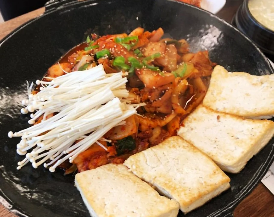 한국 식당의 커다란 무쇠 철판 위에 빨간 양념의 닭갈비와 양배추, 고구마, 떡이 함께 볶아지고 있는 근접 촬영 컷