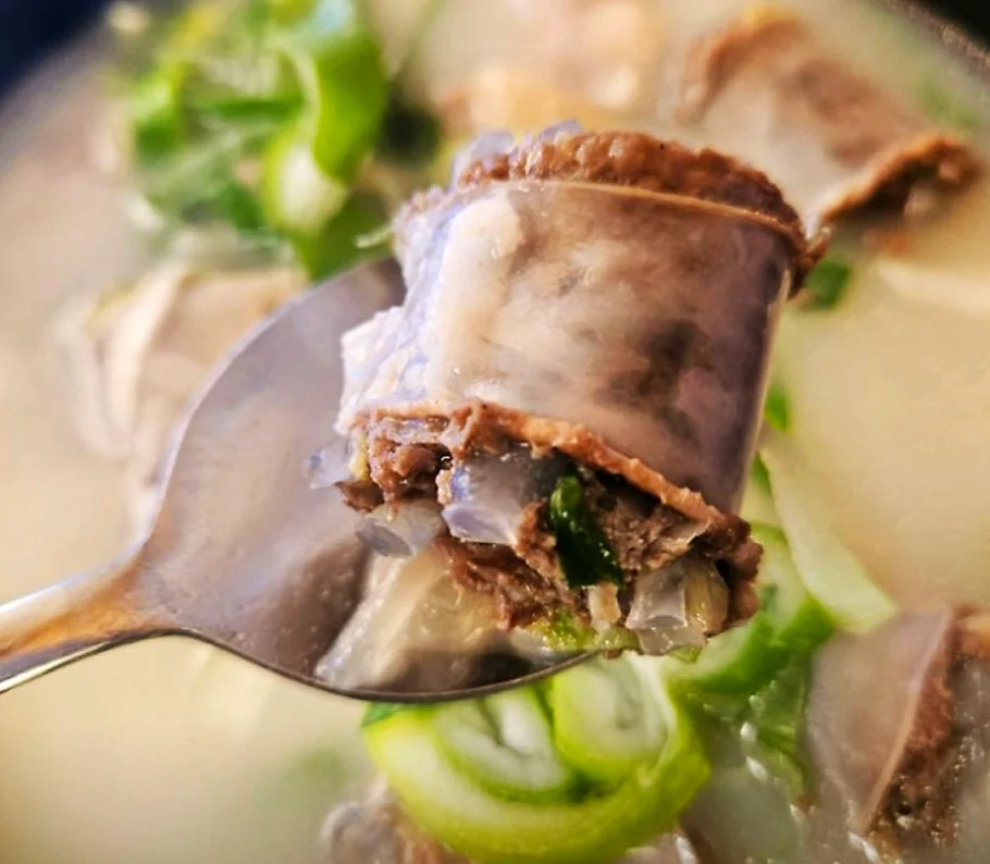 한국 식당의 석쇠 위에서 숯불에 노릇하게 구워지고 있는 닭갈비 조각들과 그 옆에 놓인 마늘, 고추 구이 장면