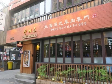 한국의 현대적인 이자카야 내부 모습으로, 나무 소재의 바 테이블과 은은한 노란 조명이 비치는 정갈한 분위기